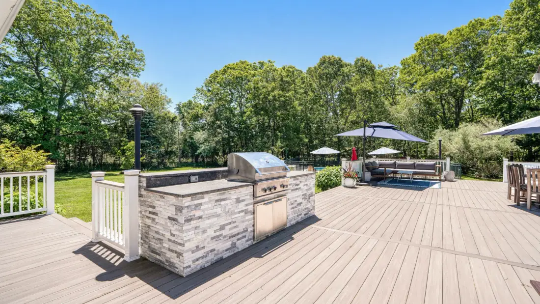Una terraza exterior cuenta con una parrilla empotrada y asientos bajo una sombrilla grande.