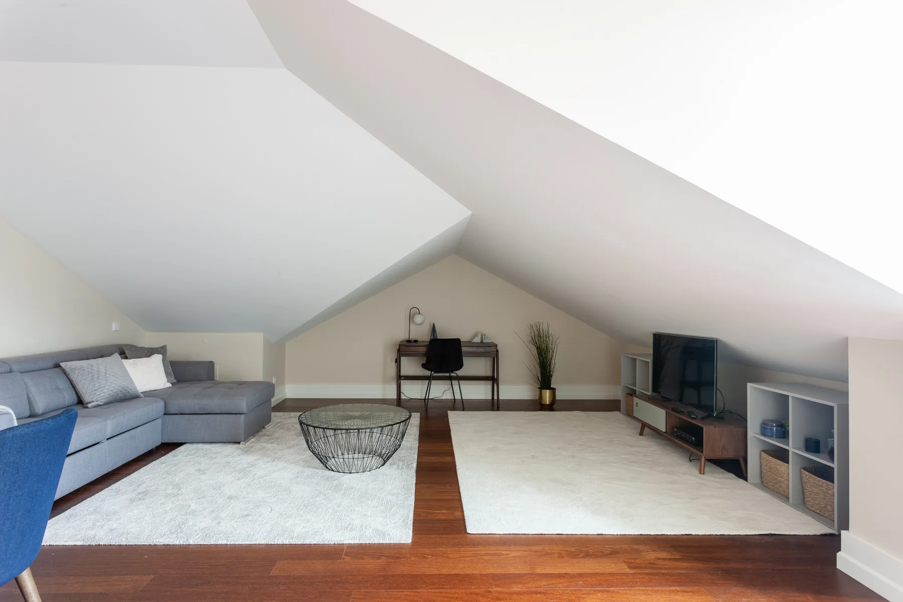 Attic living area with seating, a television, and a desk beneath sloped ceilings.