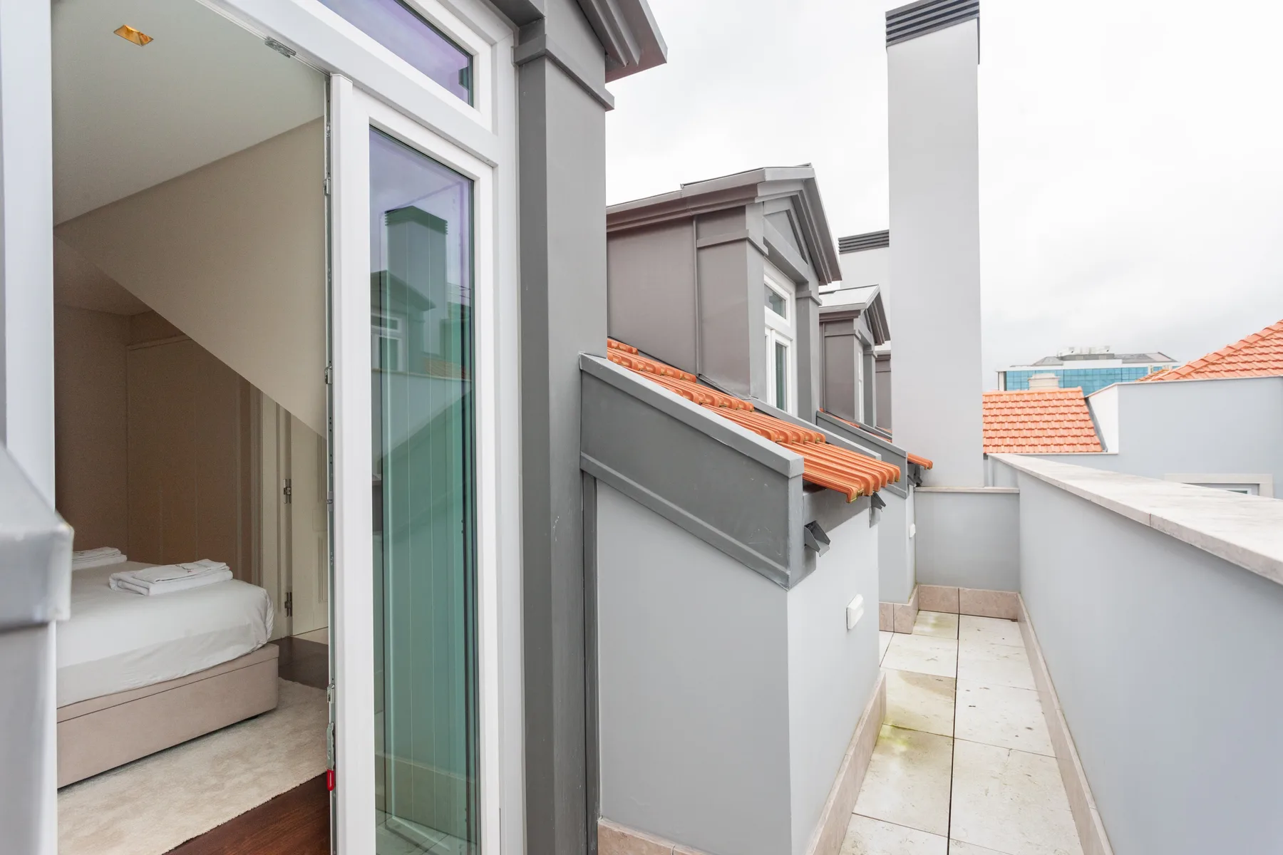 A narrow rooftop terrace runs alongside a room with an open glass door.