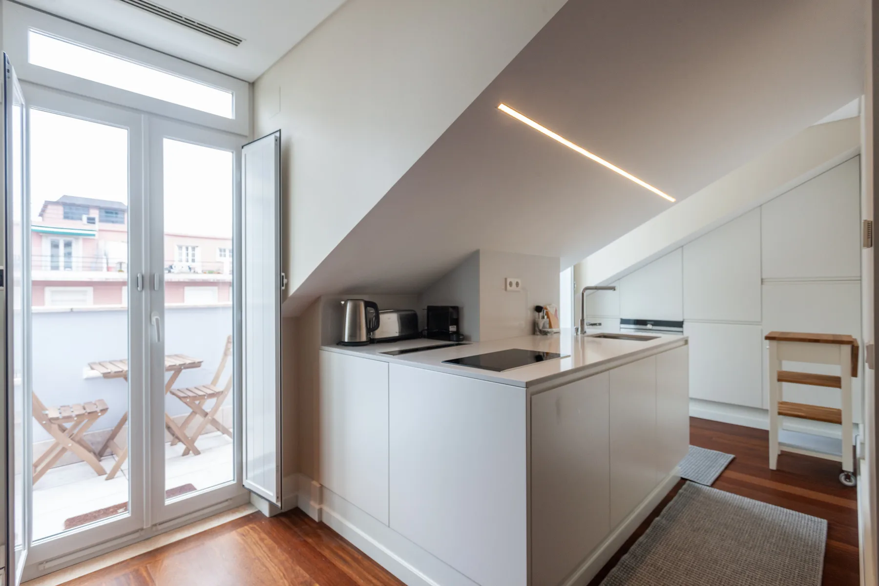 A bright kitchen with white cabinets opens onto a balcony through glass doors.