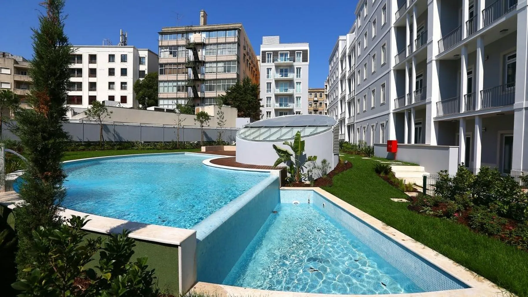 An outdoor swimming pool with a smaller connected pool beside apartment buildings.