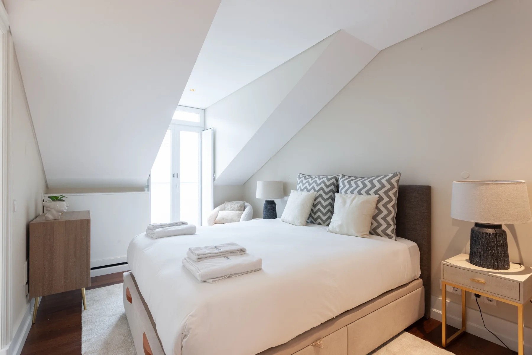 A bright bedroom with a neatly made bed and patterned pillows.