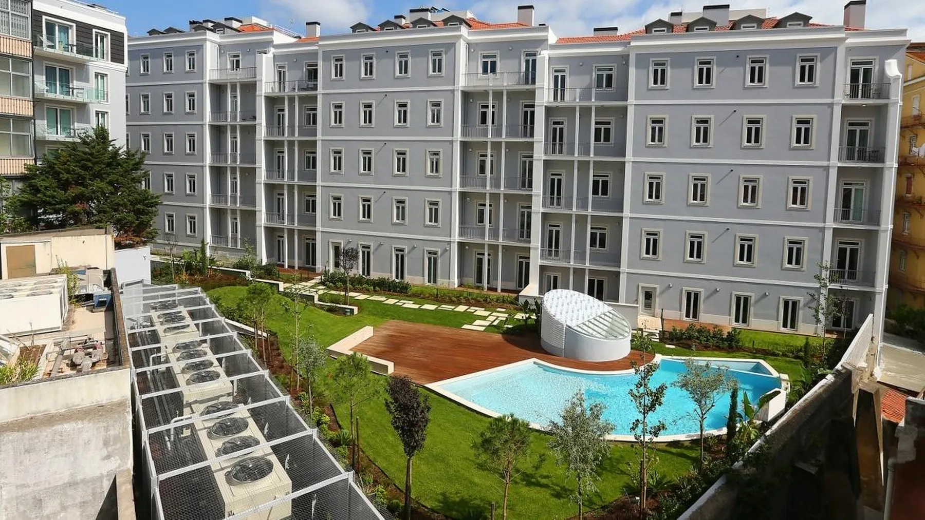 A landscaped courtyard with a swimming pool sits beside a large apartment building.