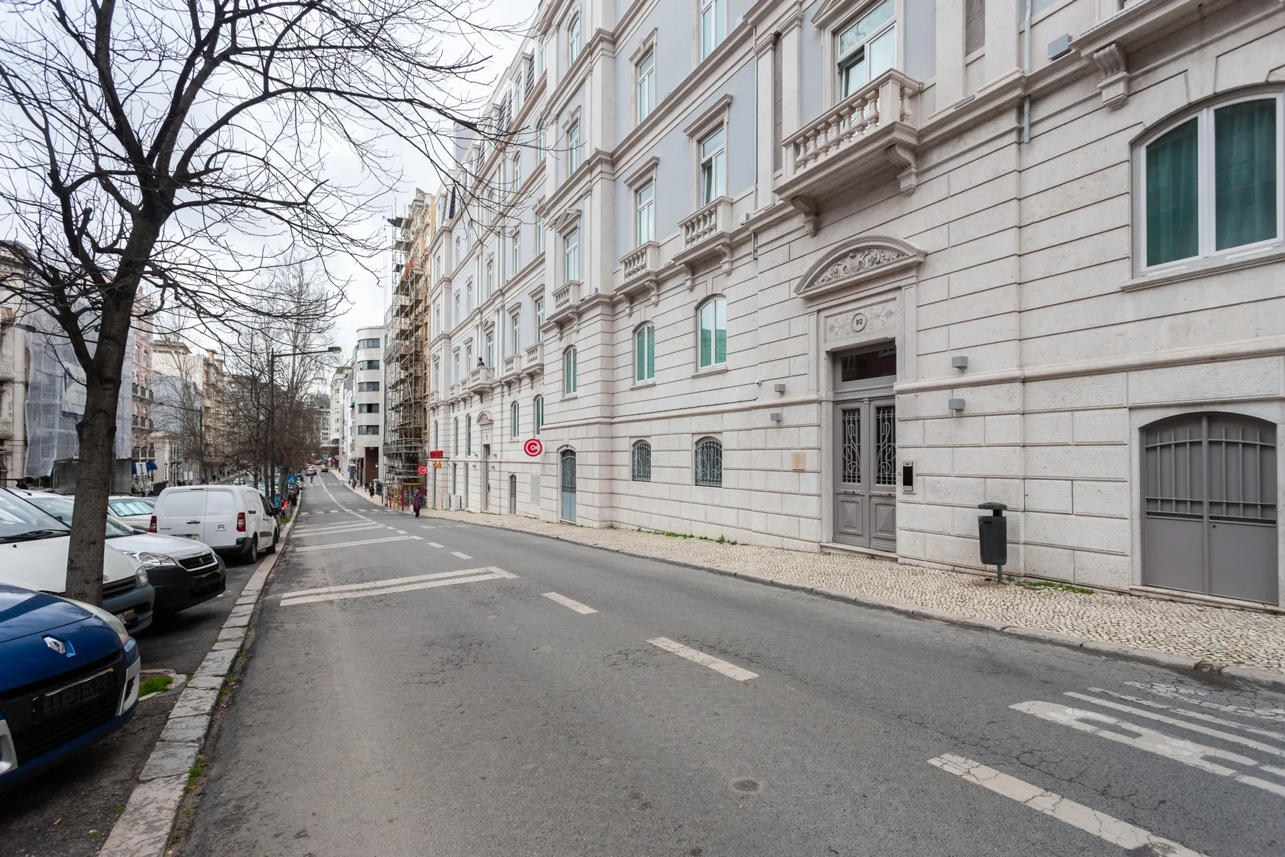 A city street lined with parked cars and a large stone-faced building.