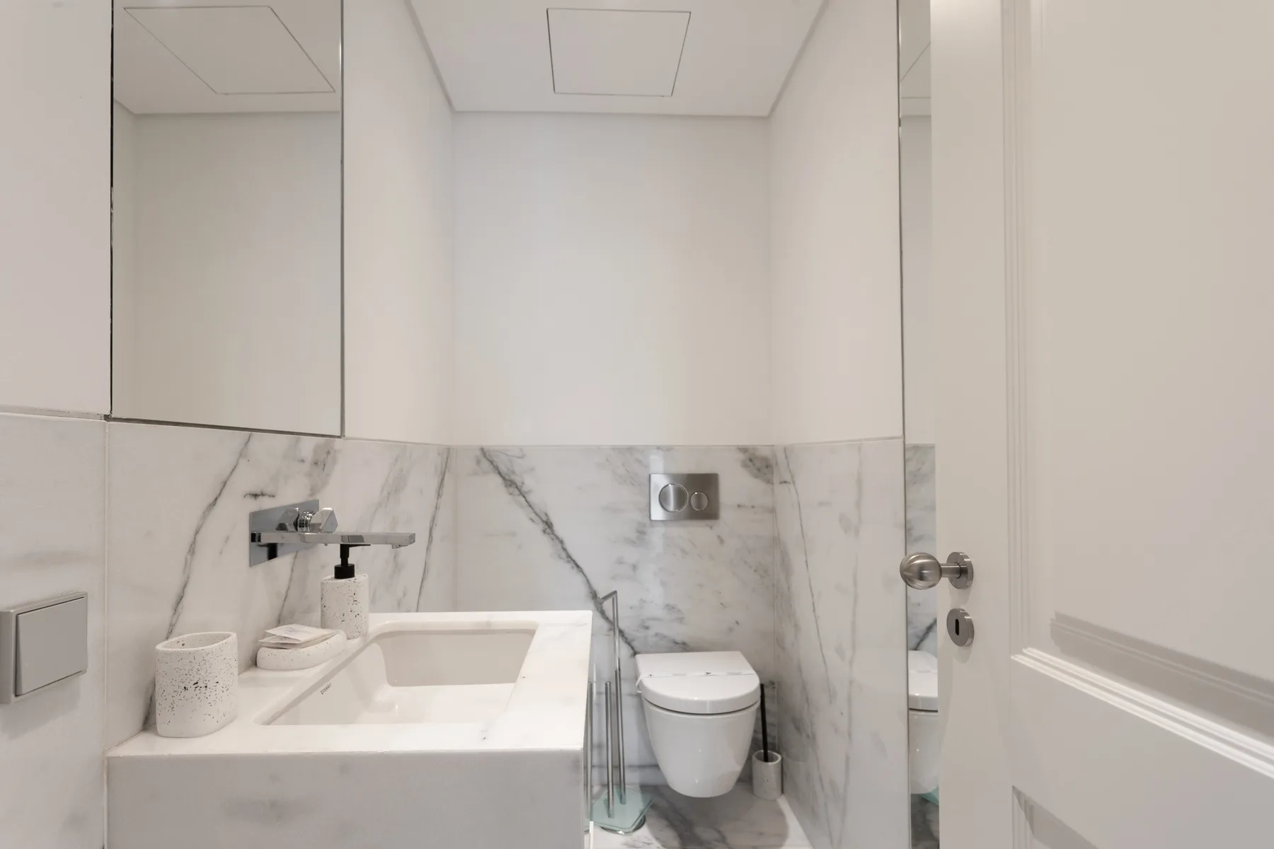 A bright bathroom with a sink, toilet, and marble-patterned wall tiles.