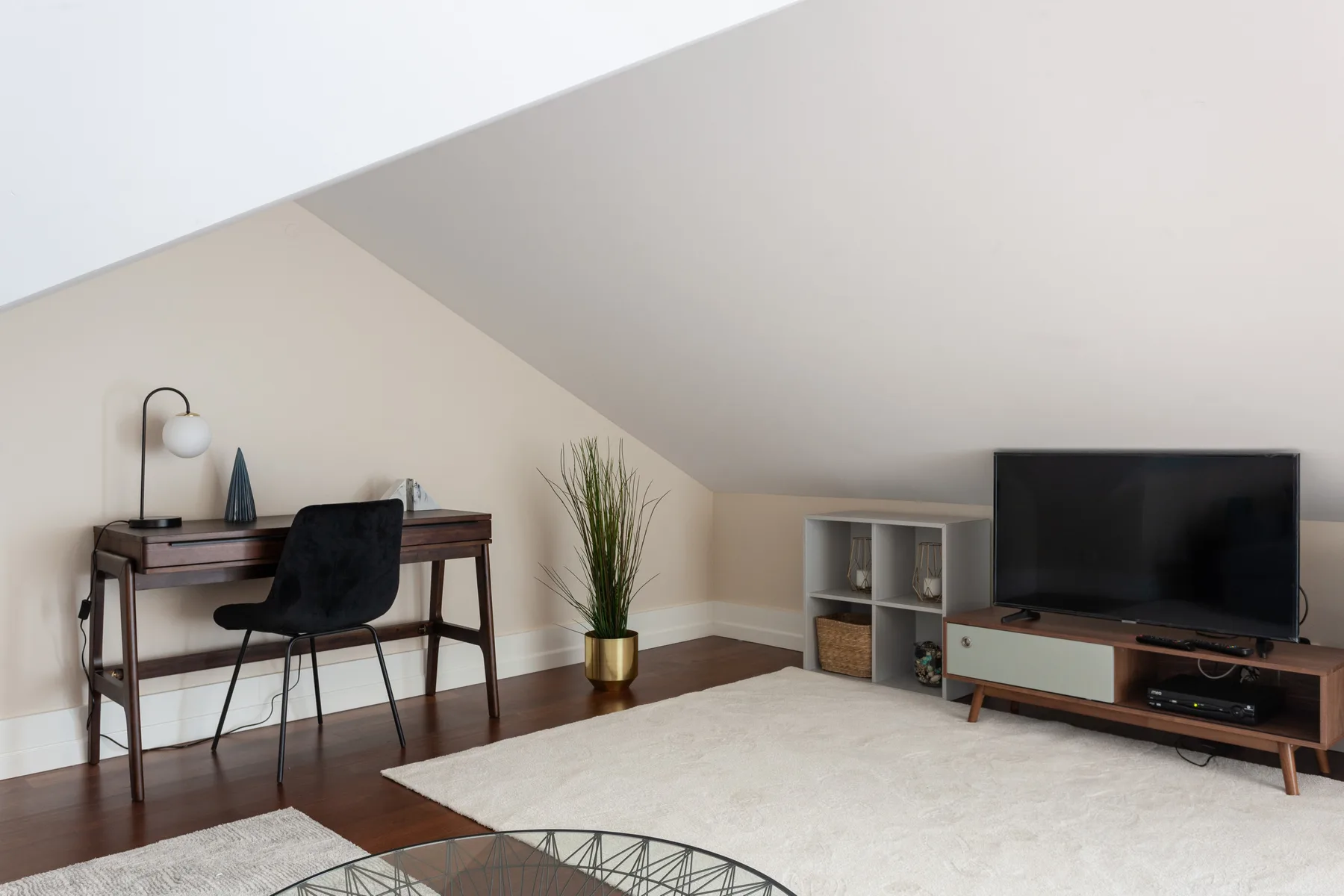 A living room with a television, seating, and a desk beneath a sloped ceiling.