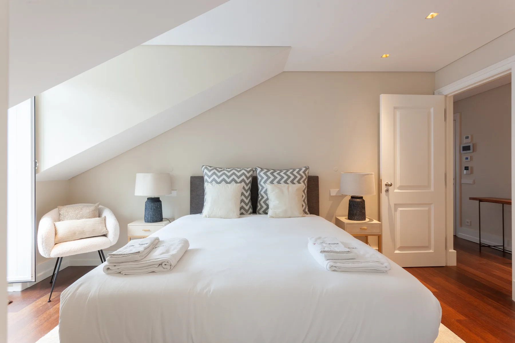 A bright bedroom with a large bed, bedside lamps, and a sloped ceiling.