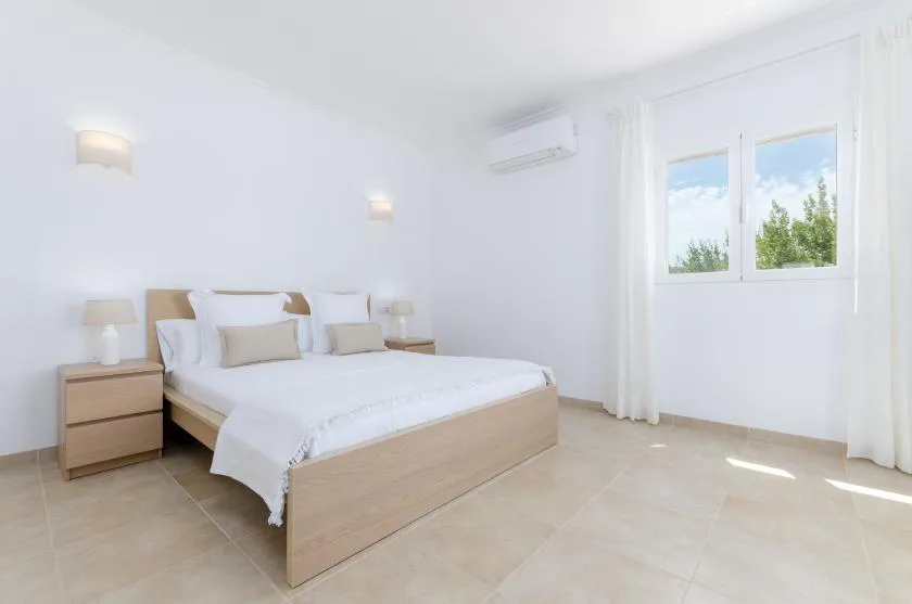 Un dormitorio luminoso con una cama bien hecha y una ventana con vistas a la vegetación.