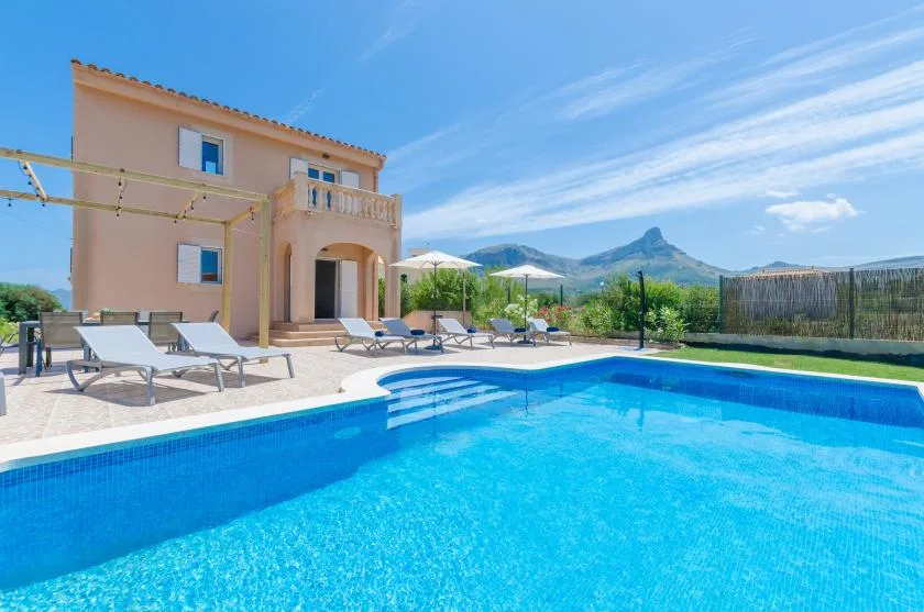 Una piscina junto a una villa, con asientos de descanso y montañas a lo lejos.