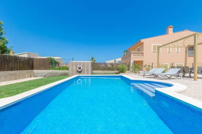 Una piscina al aire libre junto a una casa, con asientos de descanso en el patio.
