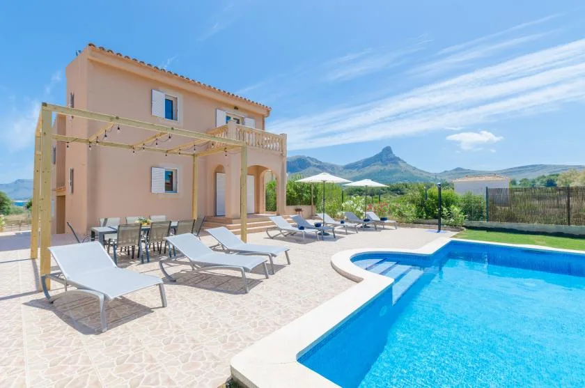 Patio de una villa con asientos al aire libre junto a una piscina y montañas a lo lejos.