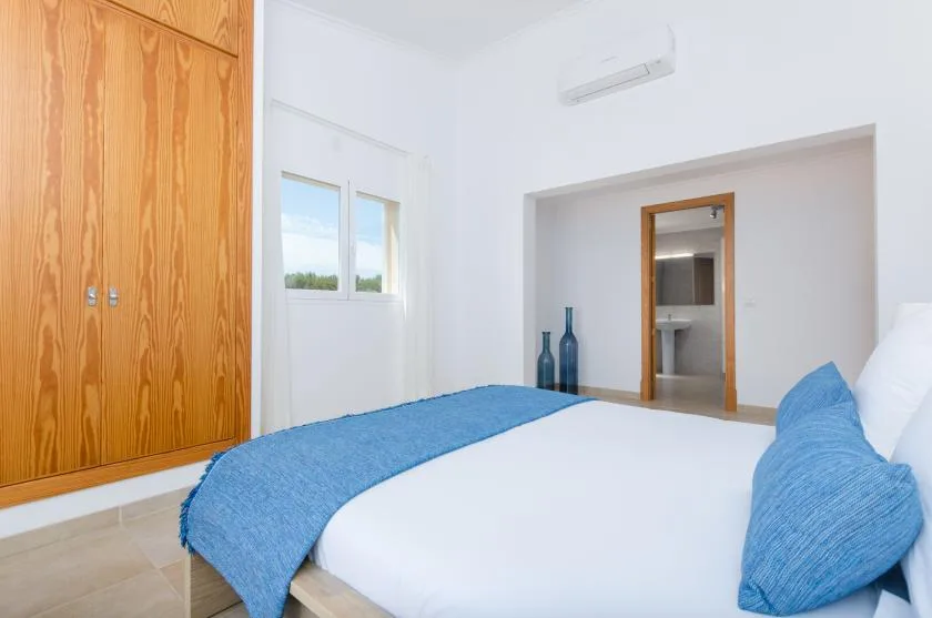 Un dormitorio luminoso con ropa de cama blanca, detalles azules y armarios de madera.