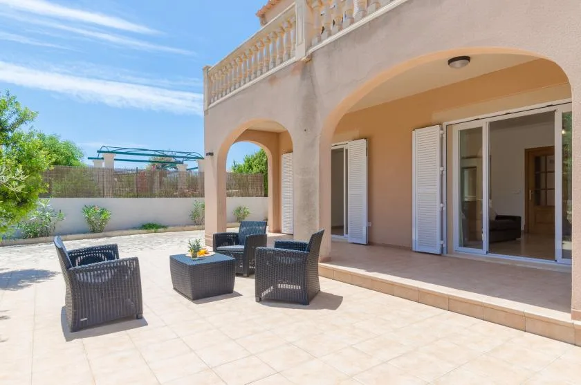 Un patio soleado con asientos al aire libre junto a una terraza cubierta con arcos.