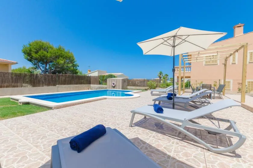 Una terraza soleada con piscina, tumbonas y una gran sombrilla blanca.