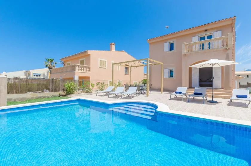 Una piscina está junto a una casa, con tumbonas en el patio de alrededor.