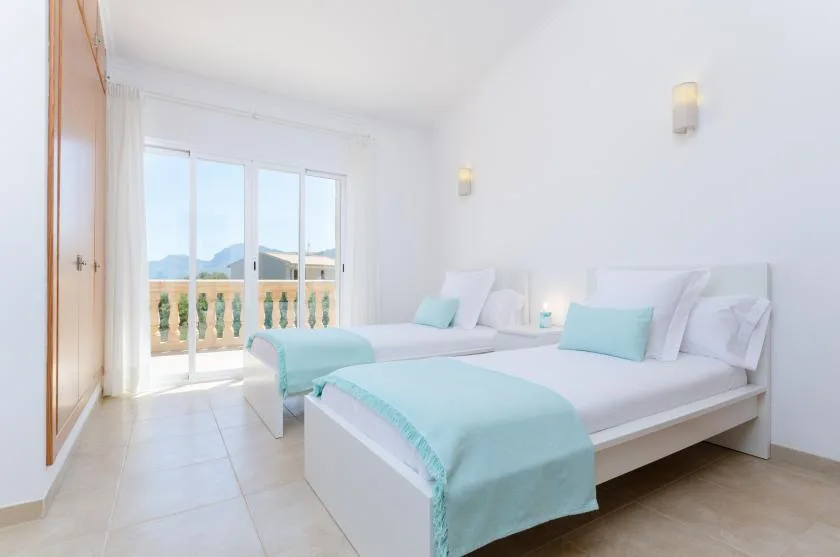 Un dormitorio luminoso con dos camas vestidas con ropa de cama blanca y turquesa.