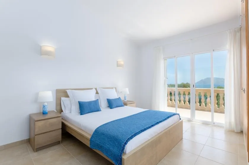 Un dormitorio luminoso con una cama vestida con ropa de cama blanca y azul.