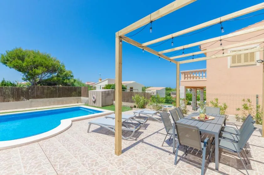 Un patio soleado junto a una piscina, con asientos al aire libre y una mesa de comedor.