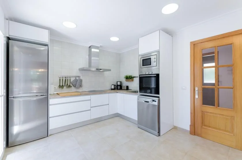 Una cocina luminosa con gabinetes blancos, electrodomésticos de acero inoxidable y una puerta de madera.