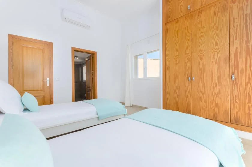 Un dormitorio luminoso con camas, ropa de cama verde agua y puertas de madera.