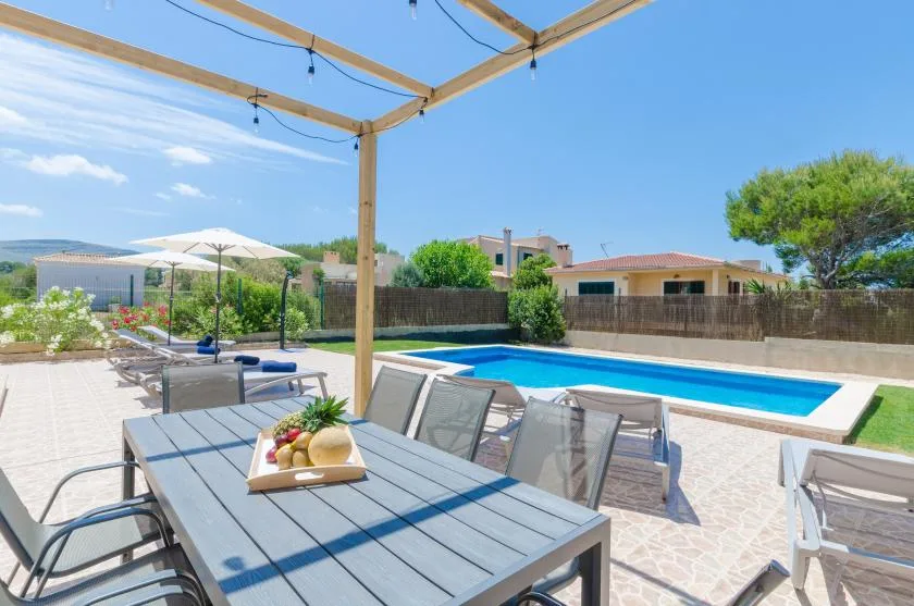 Una zona de comedor en el patio da a una piscina, con asientos al aire libre bajo una pérgola de madera.