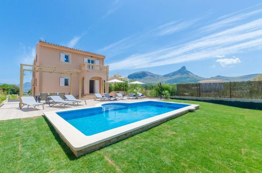 Una casa junto a una piscina y un césped, con montañas al fondo.