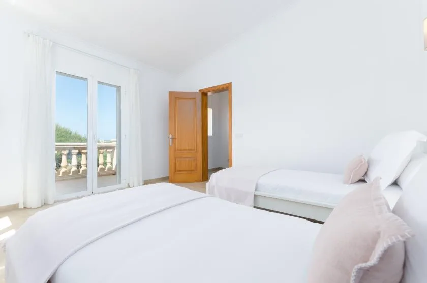 Un dormitorio luminoso con dos camas y una puerta de vidrio que da a un balcón.