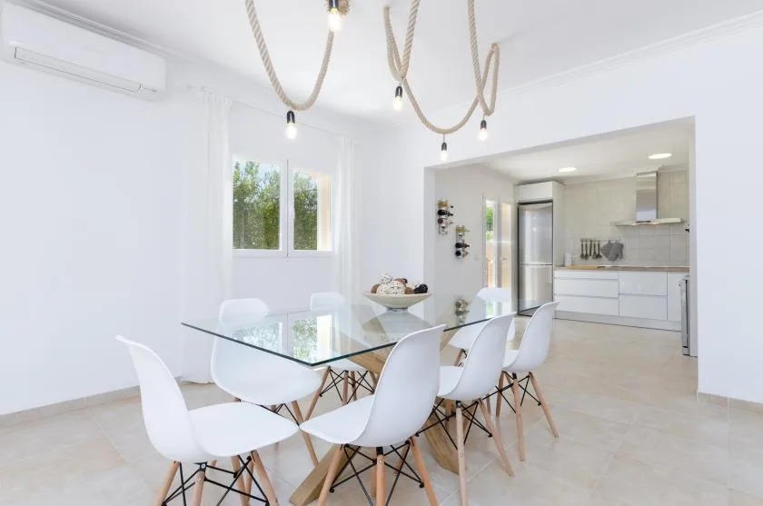 Un comedor luminoso con una mesa de cristal y una cocina abierta al fondo.