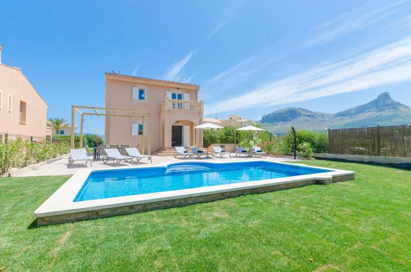 Una piscina está en un jardín con césped junto a una casa.