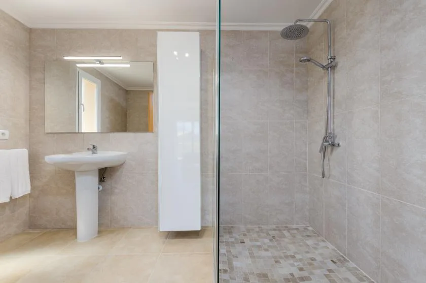 Un baño con azulejos, espejo de pared, lavabo con pedestal y ducha.