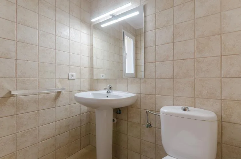 Un baño con azulejos, lavabo de pedestal, espejo e inodoro.