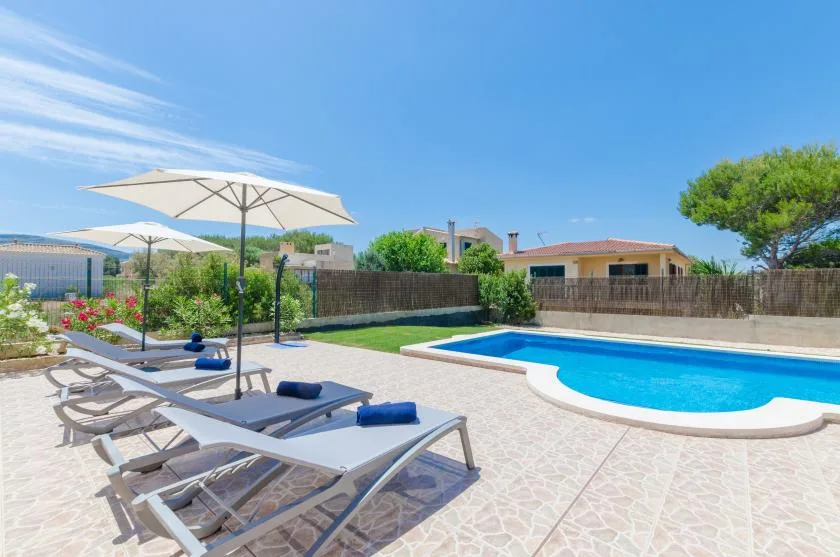 Una piscina al aire libre junto a un patio embaldosado con tumbonas y sombrillas.