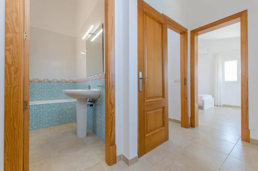 Un pasillo con puertas de madera abiertas que dan a un baño y una habitación luminosa.