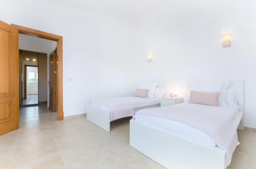 Un dormitorio luminoso con dos camas, ropa de cama blanca y suelo de baldosas claras.