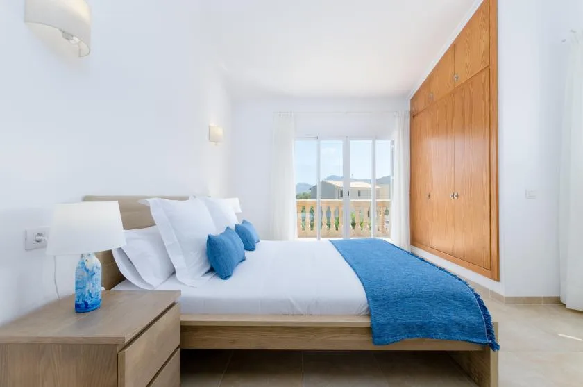 Un dormitorio luminoso con una cama vestida de blanco y azul junto a armarios empotrados de madera.