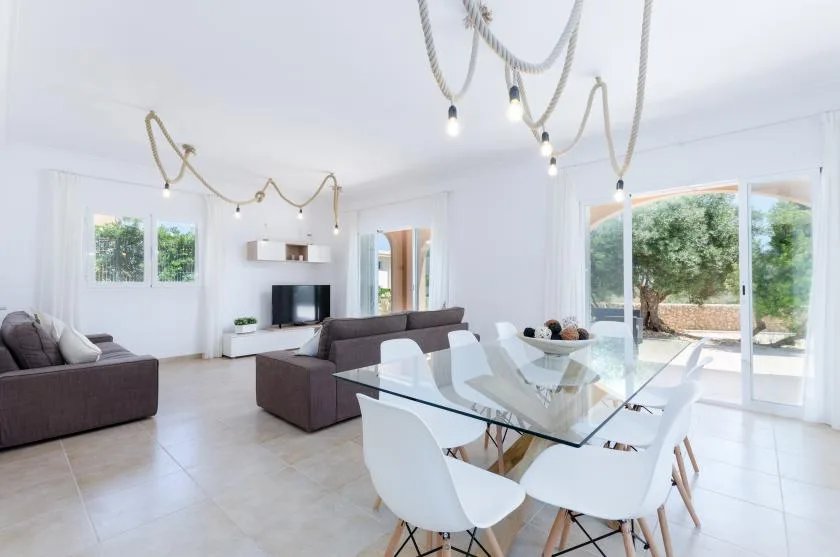 Una luminosa sala de estar y comedor con asientos, una mesa de cristal y grandes ventanales.