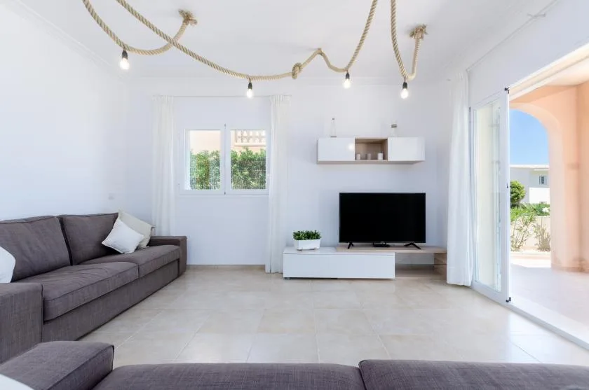 Una sala de estar luminosa con asientos y un televisor junto a la pared del fondo.