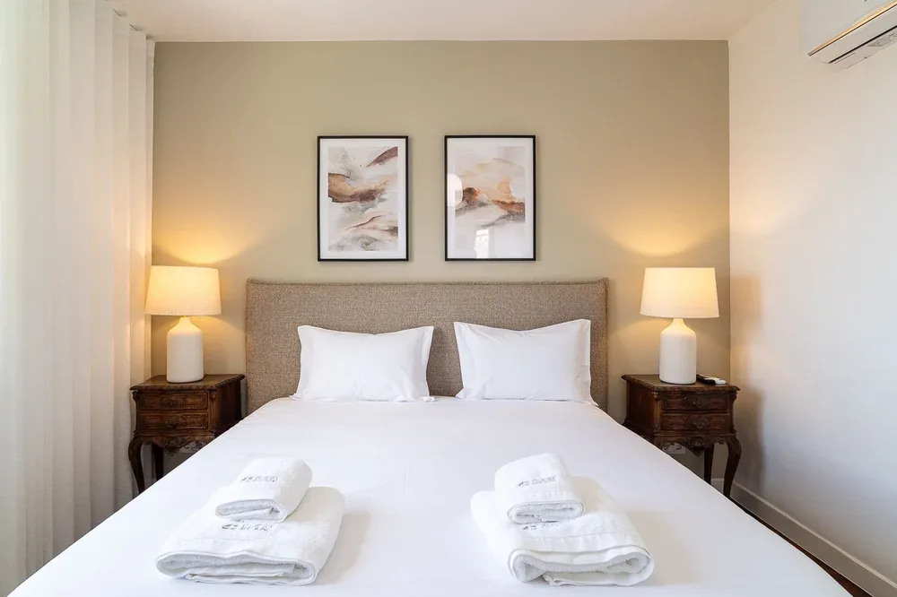 Un dormitorio con una cama bien hecha, cuadros enmarcados y lámparas de mesilla.
