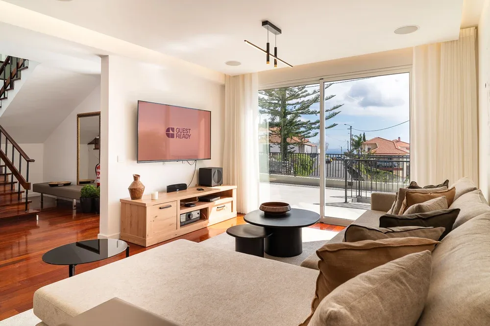 Una sala luminosa con televisor, asientos y grandes puertas de vidrio que dan a un balcón.