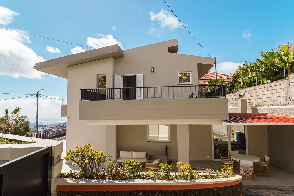 Una casa moderna de dos plantas con balcón y asientos al aire libre.