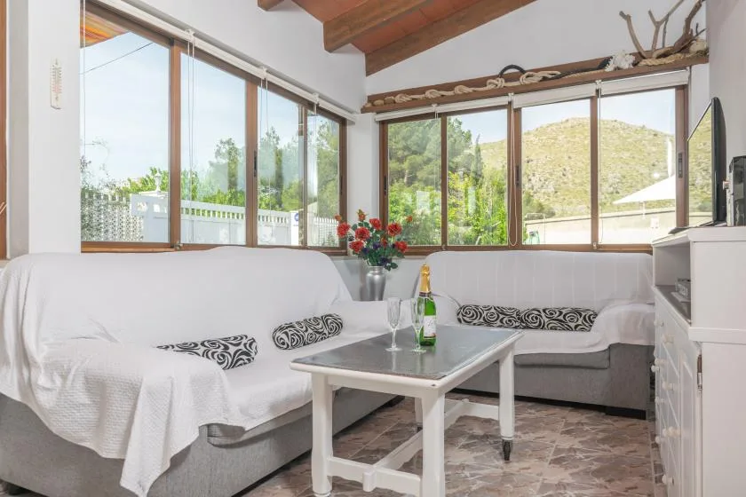 A living room with seating around a coffee table and large windows overlooking greenery.