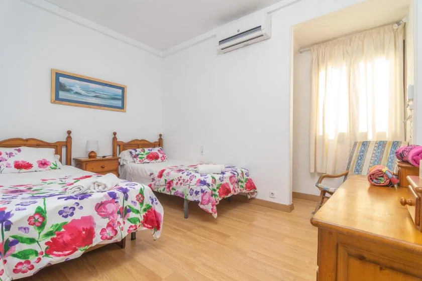 A bedroom with floral bedding, wooden beds, and a curtained window.