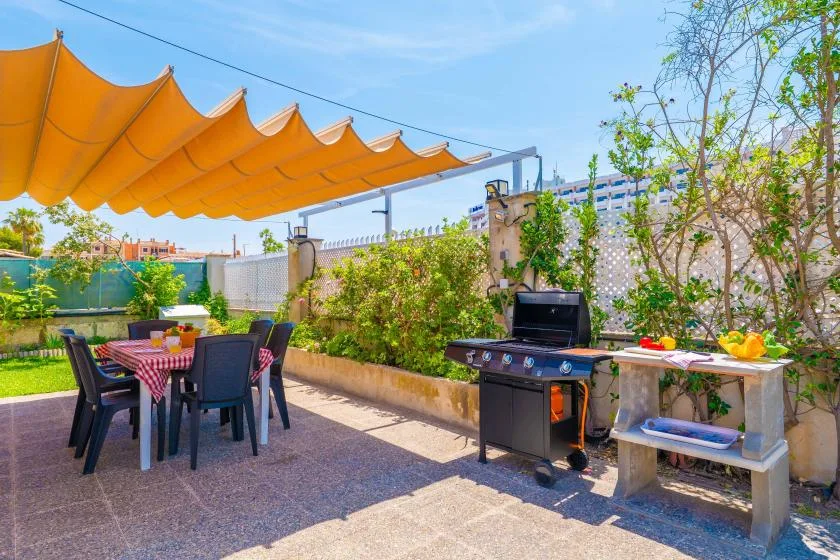 An outdoor dining and grilling area sits beneath an orange shade canopy.