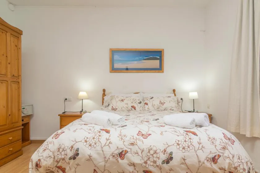 A bedroom with a floral bedspread, bedside lamps, and a framed landscape picture.