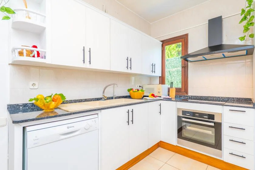 A bright kitchen with white cabinets, dark countertops, and a built-in oven.