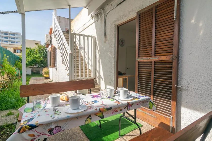 An outdoor patio table is set with cups beside an open doorway.
