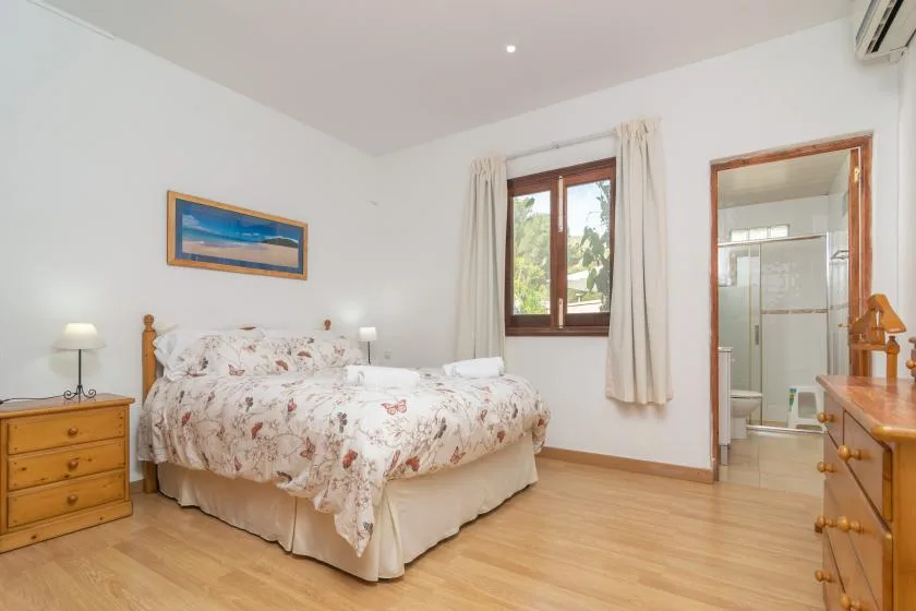 A bright bedroom with a bed, wooden dressers, and a window with curtains.