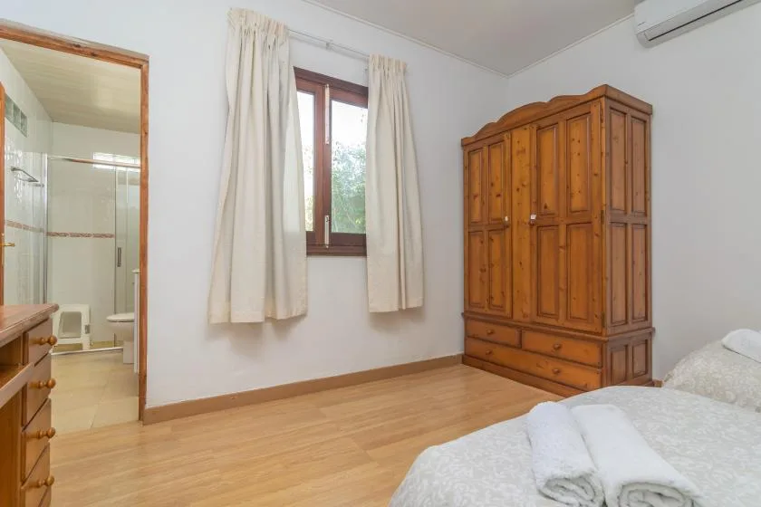 A bedroom with a wooden wardrobe, curtained window, and bed.