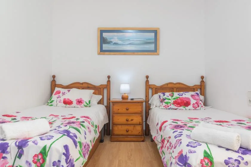 A bedroom with two beds dressed in colorful floral bedding and a nightstand between them.