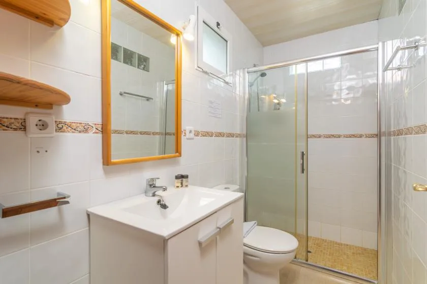 A tiled bathroom with a sink, mirror, toilet, and glass shower.